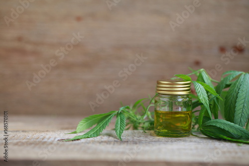 A cannabis leaf and a bottle of hemp oil on a wooden table