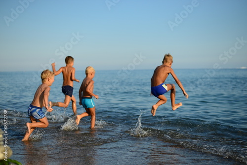 Happy children playing on the beach at the day time. Four boys frolic on the shore of the ocean. Summer vacation. Family holiday.