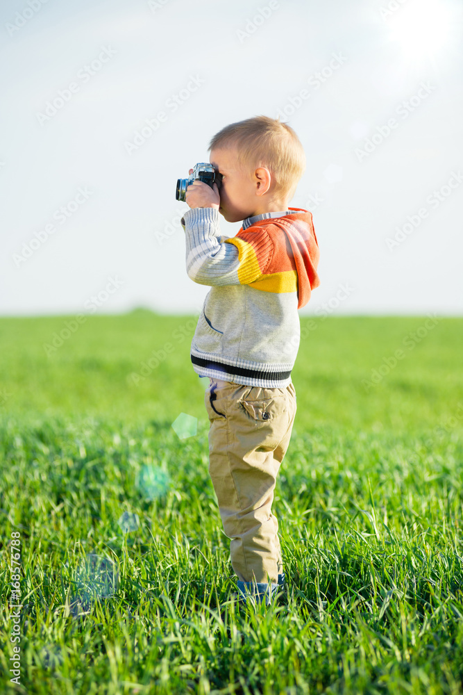 Little boy with an old camera shooting outdoor. Kid taking a photo using a vintage retro film cam. Green summer field. Little boy with an old camera shooting outdoor. Kid taking a photo using a vintage retro film cam. Green summer field.