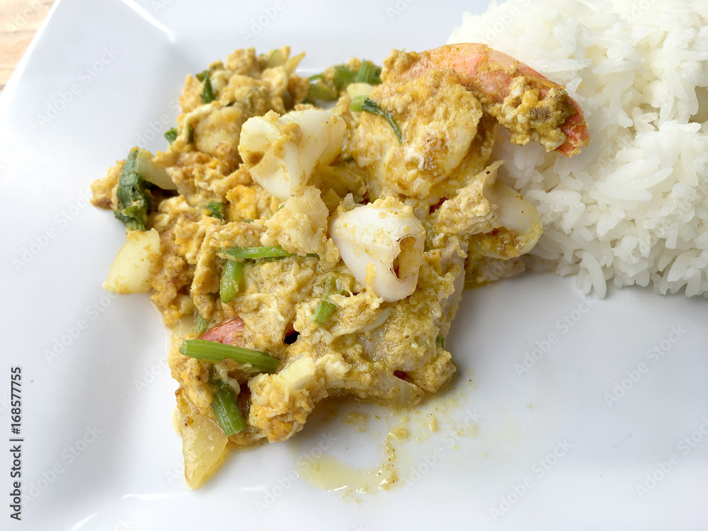 Stir-fried soft-shelled crab in curry and seafood in Curry Powder with thai jasmine rice in white dish on wooden table. (Poo-Pad-Phng-Ka-Ree Thai Food) Stir-fried soft-shelled crab in curry and seafood in Curry Powder with thai jasmine rice in white dish on wooden table. (Poo-Pad-Phng-Ka-Ree Thai Food)