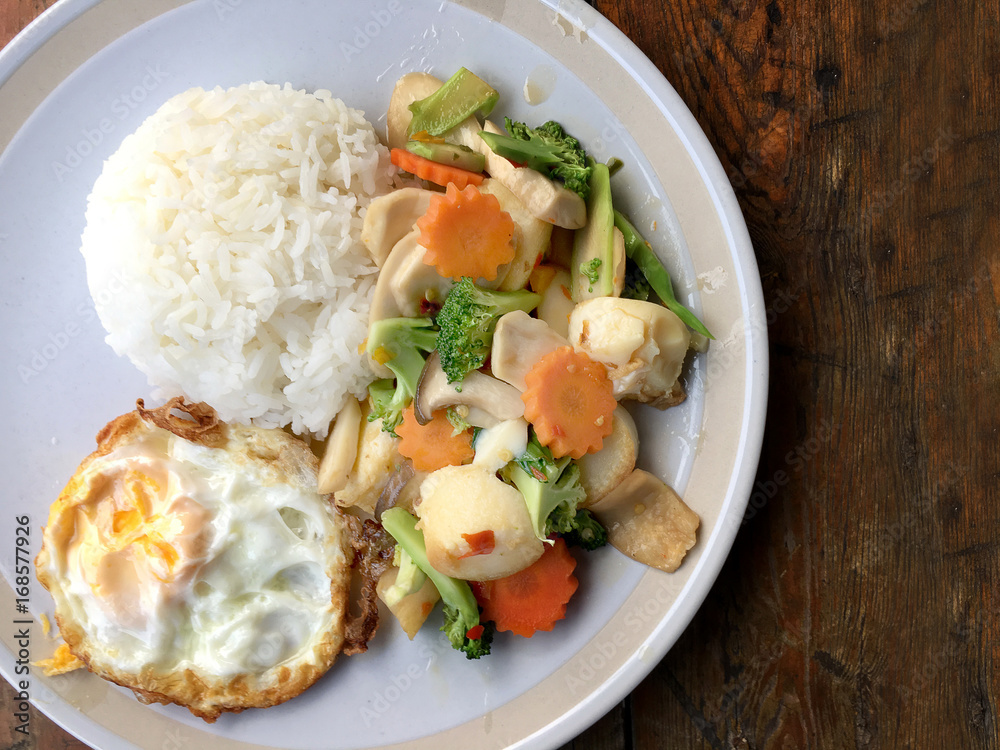 mixed fried vegetable tofu with rice and fried egg in white dish on wooden background. Vegetarian Food, healthy food.