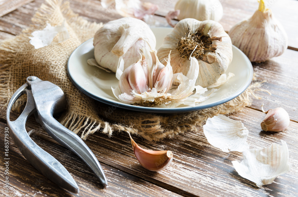 Garlic cloves and garlic bulb with metall press on wooden background. Garlic is used as seasoning and as a traditional medicine.