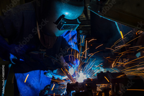 Industrial worker is welding in automotive part factory