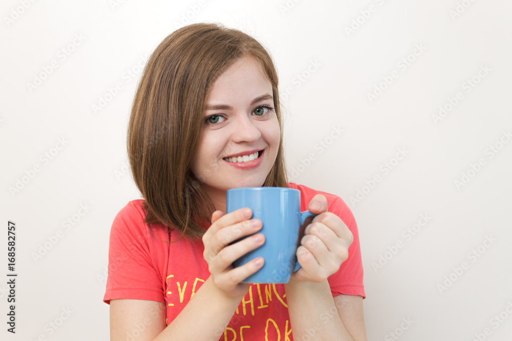 Portrait photo of smiling beautiful girl with bob haircut in red pink t-shirt holding blue cup with both hands as if saying: Good morning! or Coffee time! White background. Portrait photo of smiling beautiful girl with bob haircut in red pink t-shirt holding blue cup with both hands as if saying: Good morning! or Coffee time! White background.