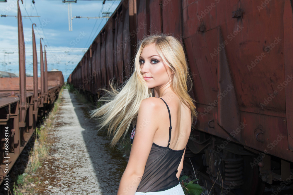 Fototapeta premium Beautiful blonde girl walking on rail tracks, romantic look, from back, wind tin the hair