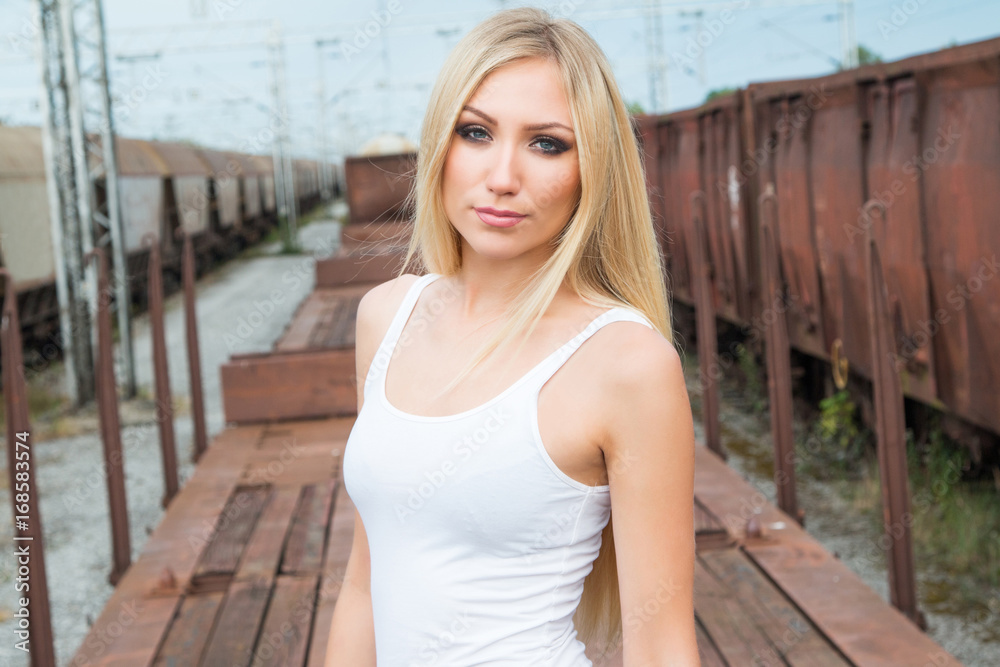 Beautiful blonde girl in white shirt standing on freight rail wagon, romantic look