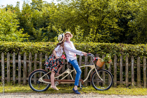 Young couple riding a bike tandem in the park. Against the background of the fence from the tree