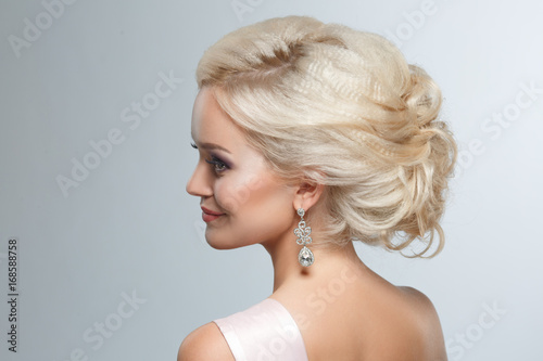 A smart wedding hairstyle on a blonde woman on a gray background.