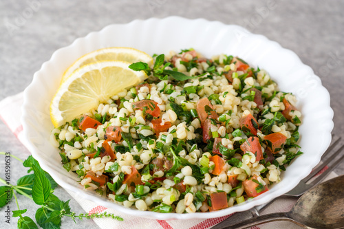 Tabbouleh salad with bulgur, tomatoes, parsley, green onion and mint in plate on grey stone table.