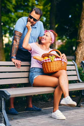 A couple is having a picnic on a bench in a park.