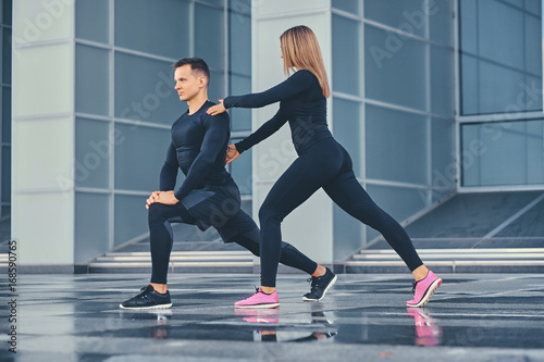 Fitness couple is stretching over modern building background.
