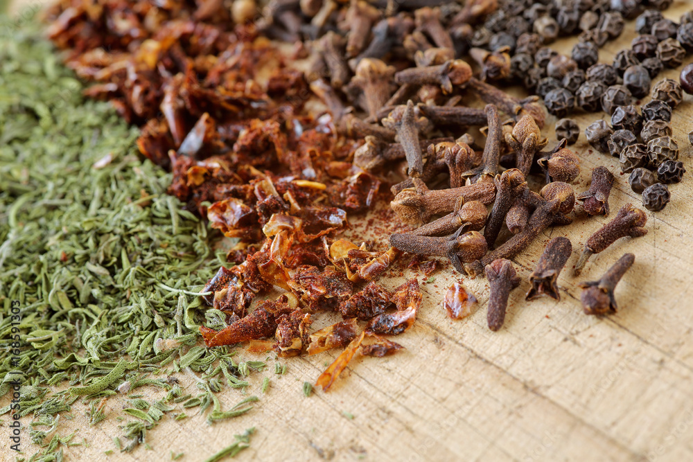 Extreme close up of herbs and spices on a wooden cutting board. Macro shot of savory, paprika, clove and pepppercorn