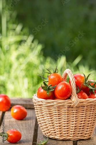 Red tomatoes in wicker basket on  wooden table.