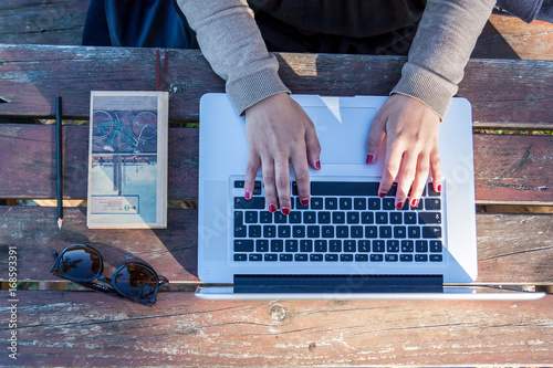 Woman working on a park on her laptop with black screen on a wood table.