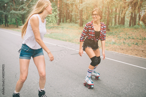 Two slim and sexy young women and roller skates. One female has an inline skates and the other has a quad skates. Girls ride in the rays of the sun