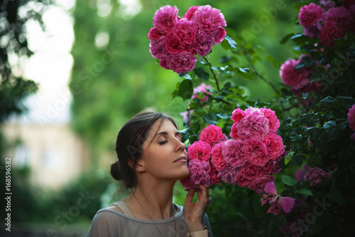 Photography Beautiful tender woman enjoying with a scent of pink roses at garden
