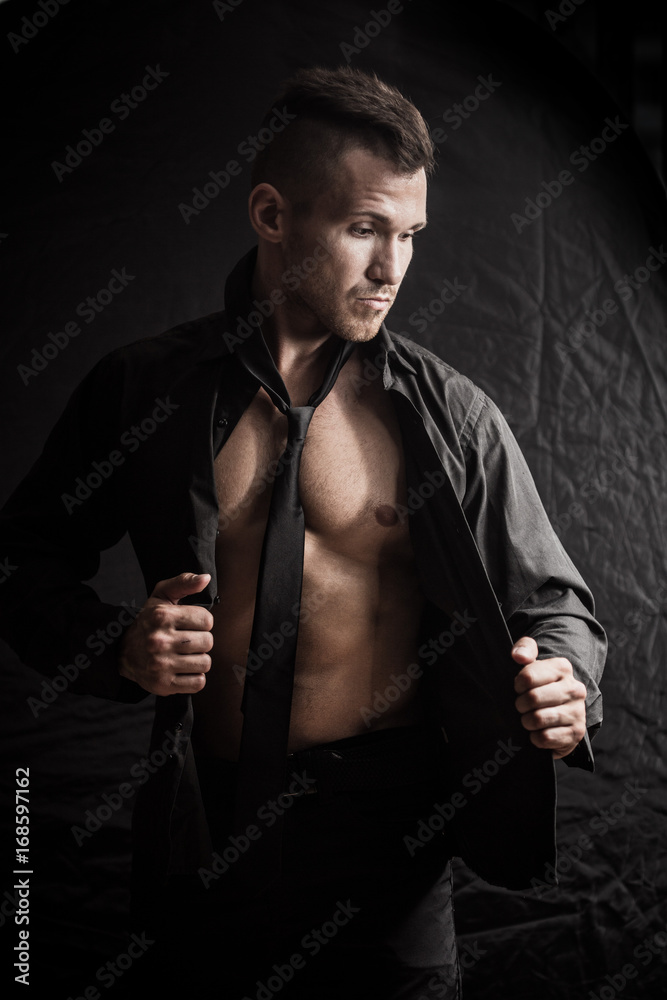 man sexually removes clothes on a dark background