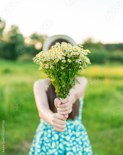 A young girl in a blue dress is holding a bouquet of wildflowers in her hands