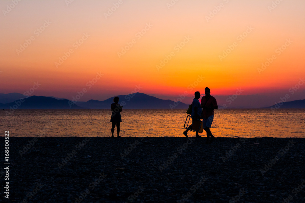 Silhouetted shot of sunset with couple, people by the beach