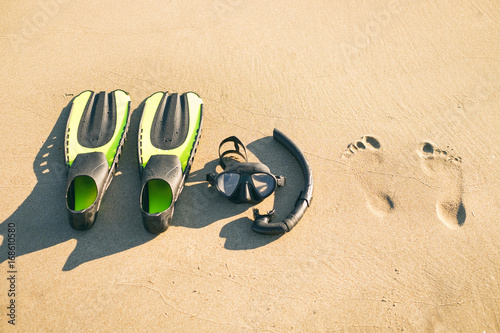 Swim flippers with snorkel, mask and feet steps on a sandy beach. Water sports. Snorkeling. Travel and holiday concept. Fins and scuba mask. photo