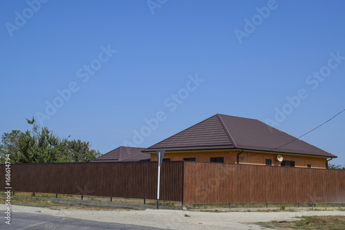 A house with a metal corrugated roof and a gauve fence made from a brown metal profile © eleonimages