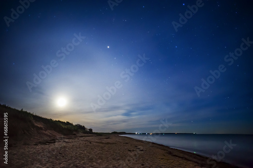 Full moon behind soft clouds glowing and casting light on beach at night