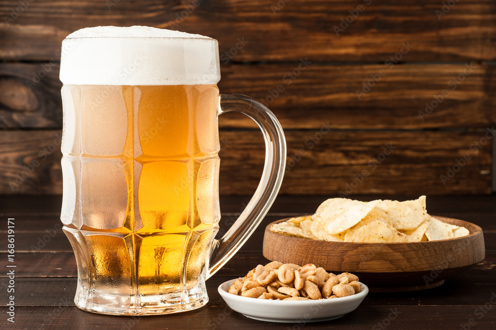 glass of cold frothy lager beer and snacks on wooden table glass of cold frothy lager beer and snacks on wooden table