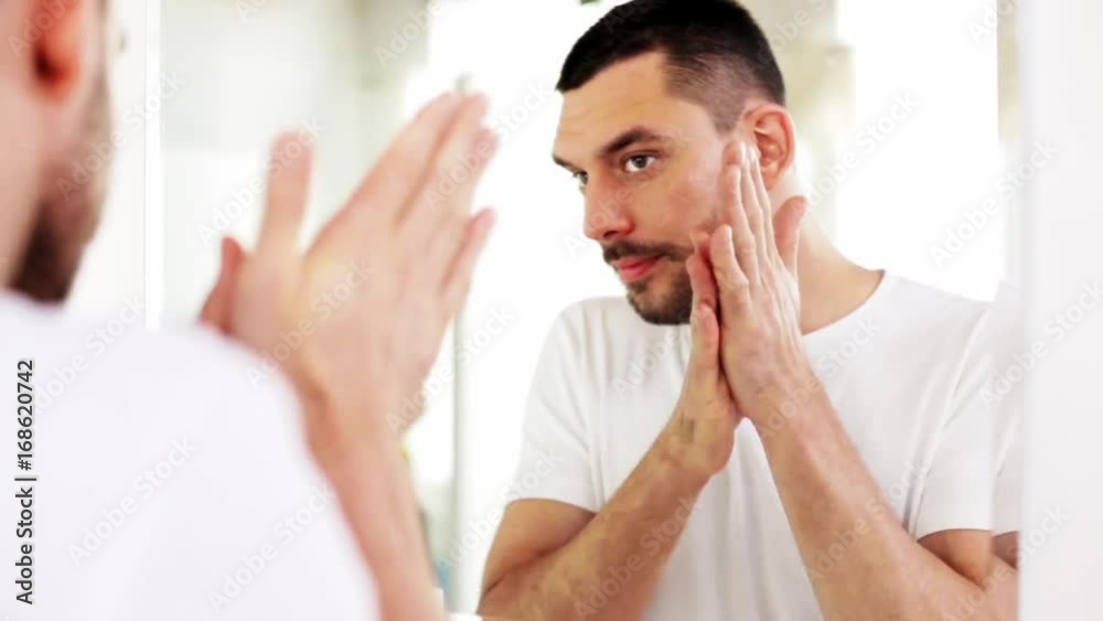 man applying after shave oil to face at bathroom man applying after shave oil to face at bathroom