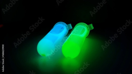 Plastic tubes with quantum dots of perovskite nanocrystals glowing with blue and green luminescence in the dark due to ultraviolet radiation photo