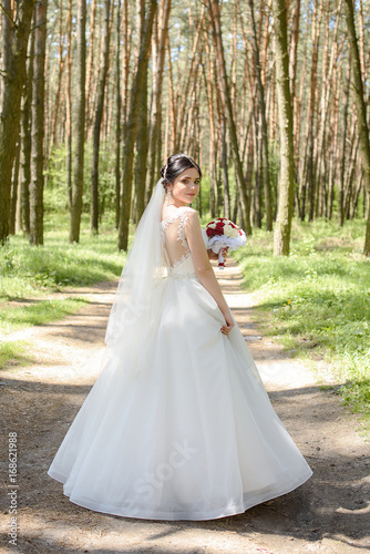 Wedding. The bride in a dress standing in a green forest and holding a Wedding bouquet of white flowers roses