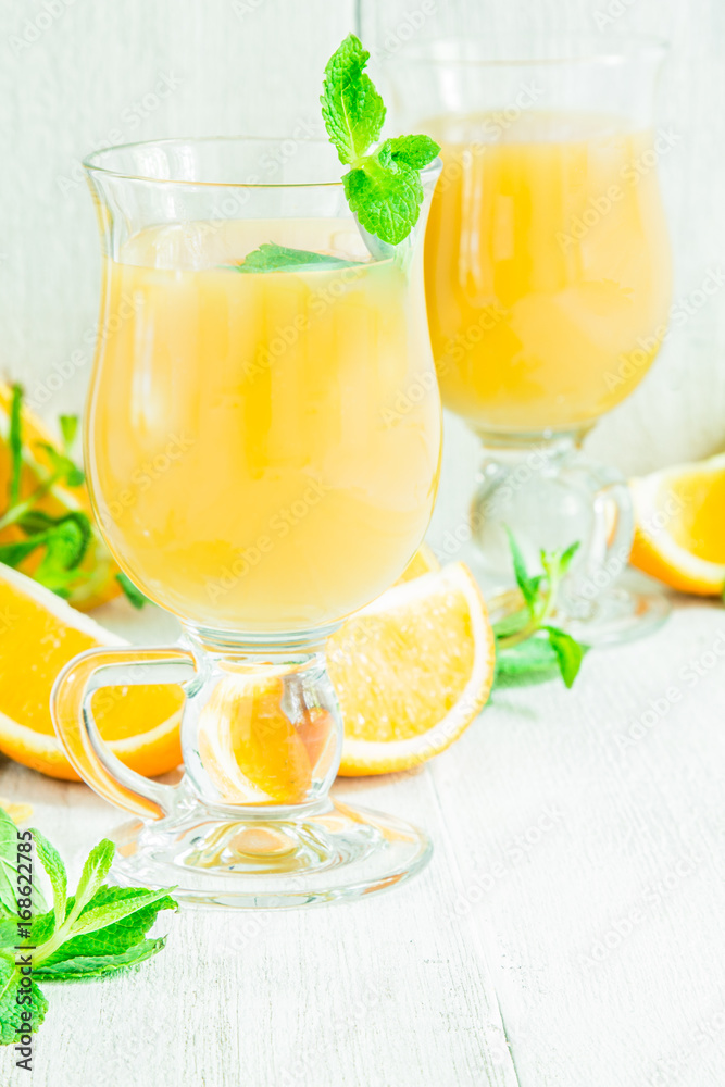 Orange juice in a glass on a white wooden table with whole and sliced oranges Orange juice in a glass on a white wooden table with whole and sliced oranges