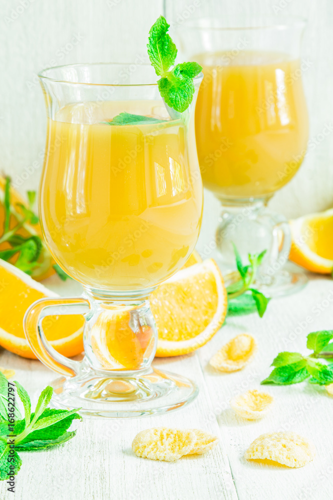 Orange juice in a glass on a white wooden table with whole and sliced ​​oranges
