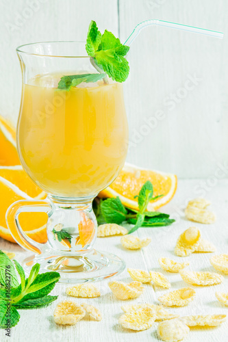 Orange juice in a glass on a white wooden table with whole and sliced ​​oranges