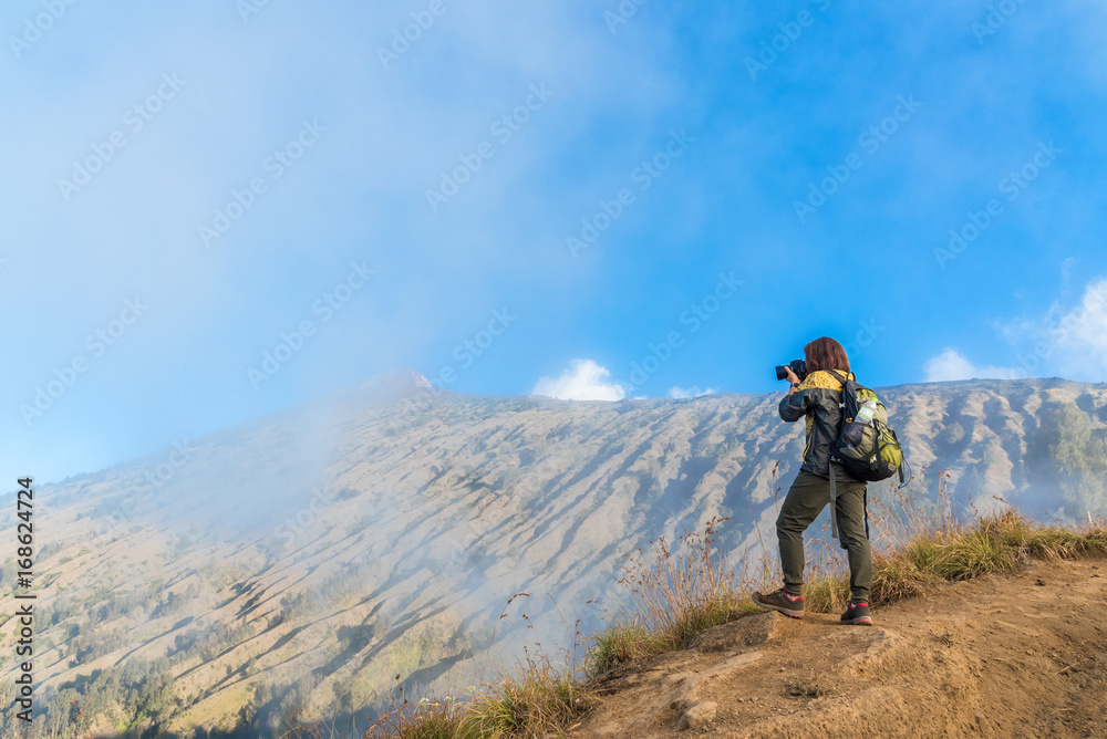 Woman hiker wear yellow and black jacket, taking photograph, enjoy and happy with mountain top view after finished climbing at mount Rinjani, Lombok, Indonesia.