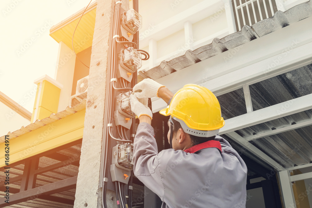 Electrician in a gray uniform wears gloves and a helmet installing a power meter on an electricity pole. Electrician in a gray uniform wears gloves and a helmet installing a power meter on an electricity pole.