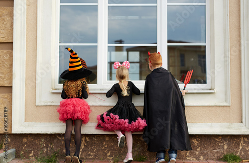 Halloween boy and girls looking through window of house from outside photo