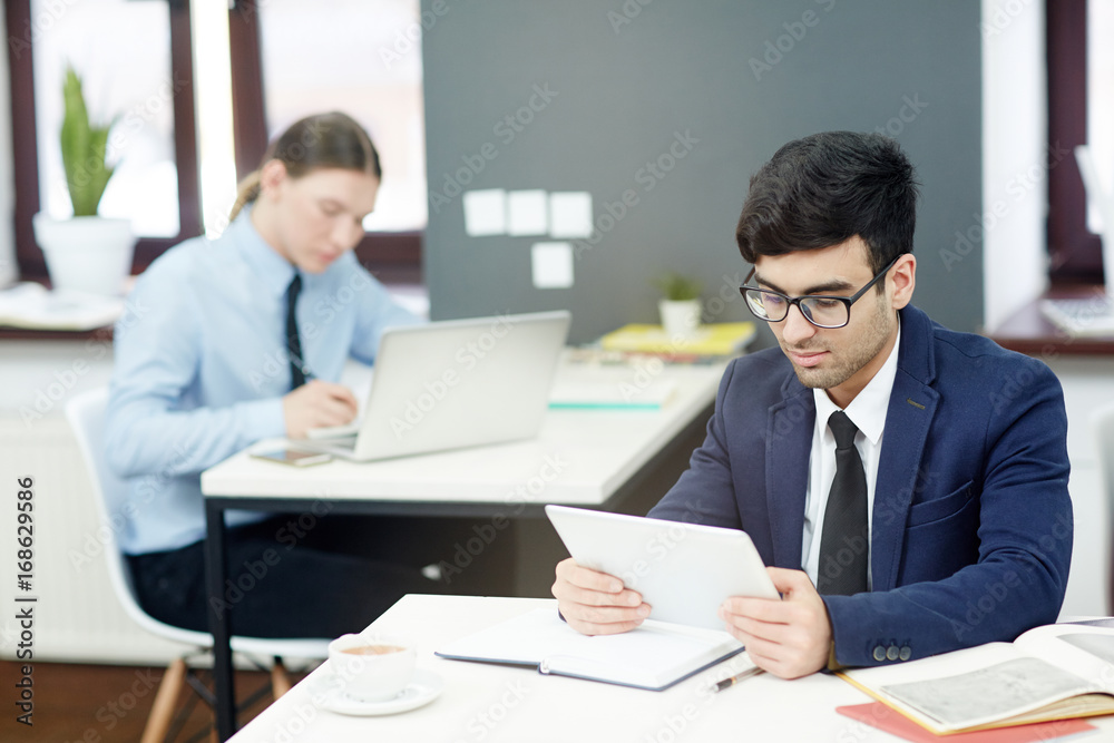 Concentrated young managers in formalwear preparing financial accounts on computers while sitting at modern open plan office