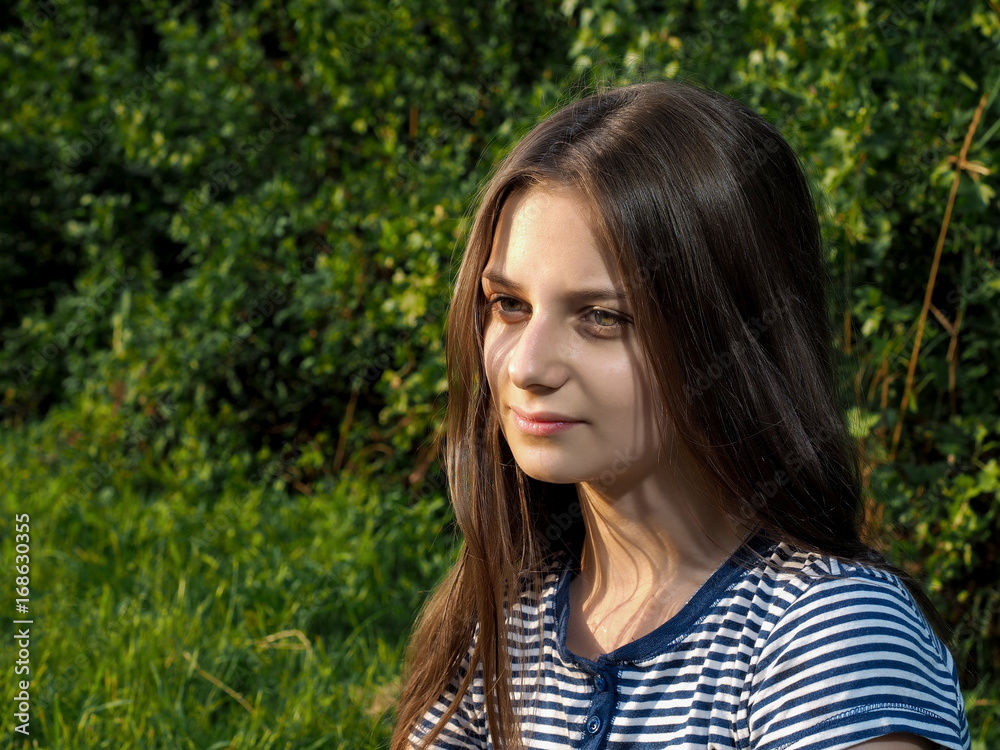 Portrait of a beautiful young girl with long brown hair. Summer, green grass, nature