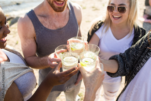 Joyful friends toasting with glasses of caipirinha at beach party