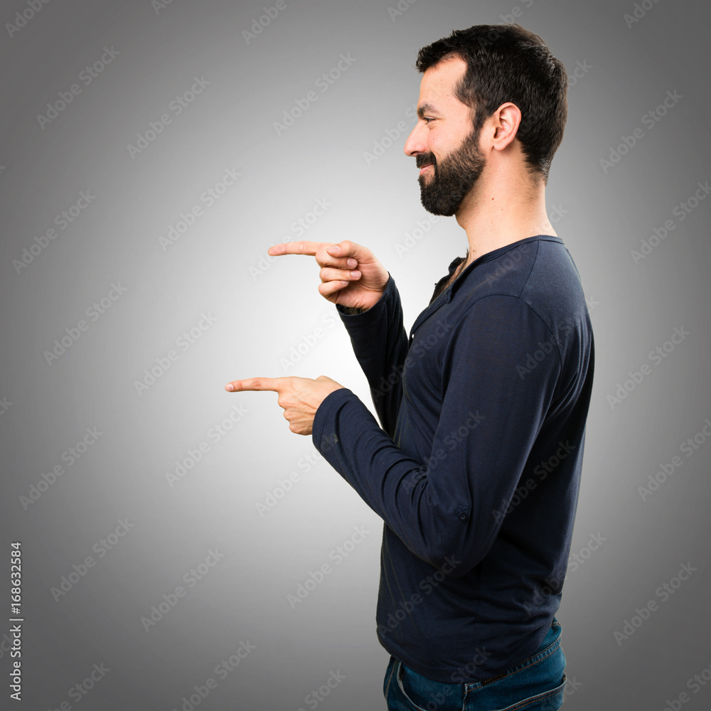 Handsome man with beard pointing to the lateral on grey background Handsome man with beard pointing to the lateral on grey background