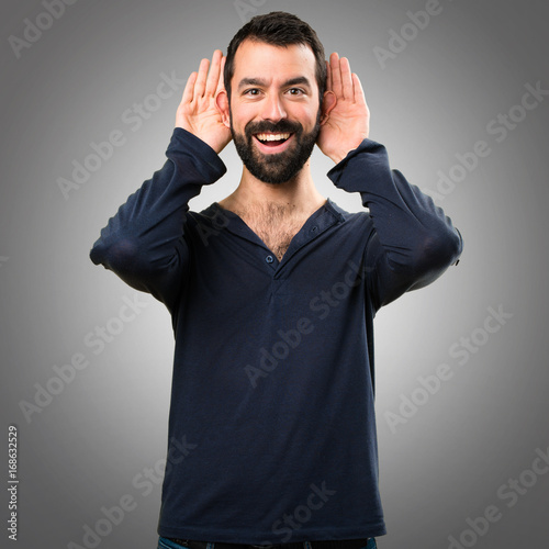 Handsome man with beard listening something on grey background