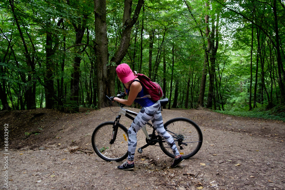 young girl in sport wear with bicycle riding in forest in summer