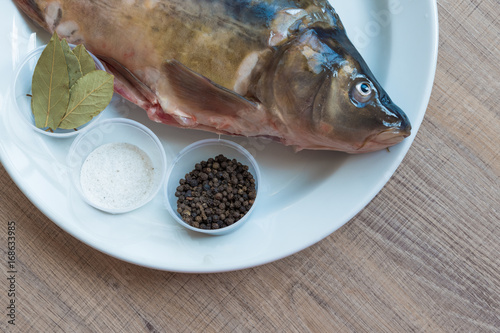 Carp with scales peeled and prepared for cooking, with spices on a white plate. photo