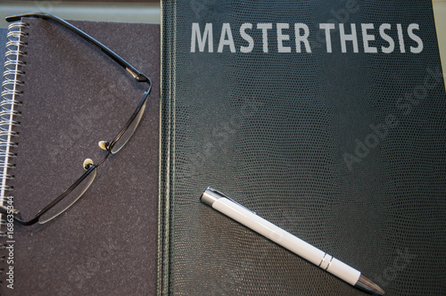 a master thesis hard cover, notepad pen and glasses photo