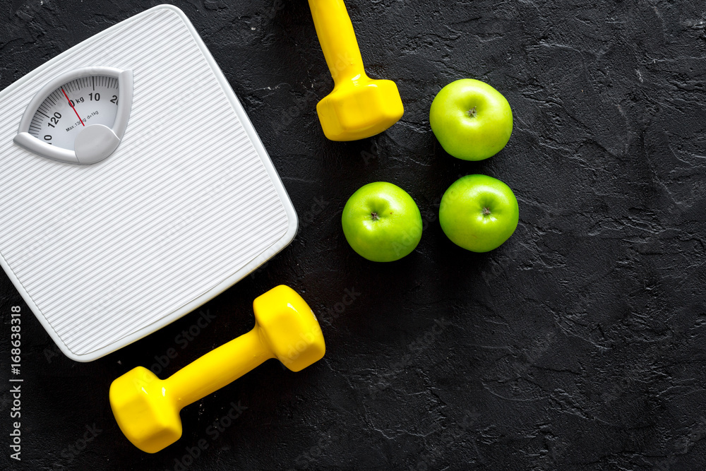 Sport and diet for losing weight. Bathroom scale, apple and dumbbell on black background top view copyspace Sport and diet for losing weight. Bathroom scale, apple and dumbbell on black background top view copyspace