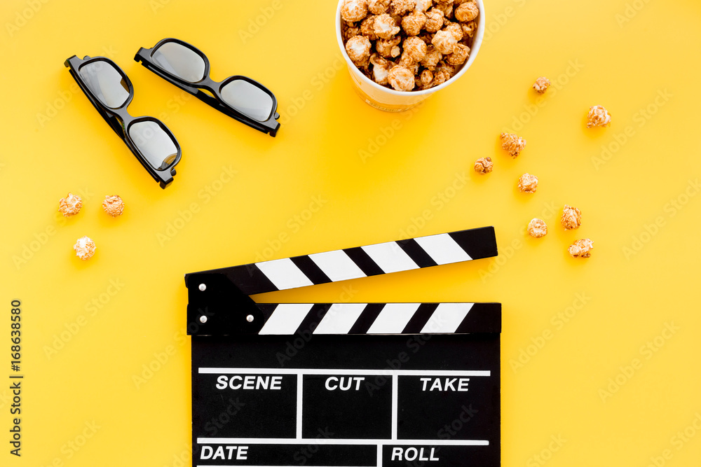 Ready to watch film. Clapperboard, glasses and popcorn on yellow background top view