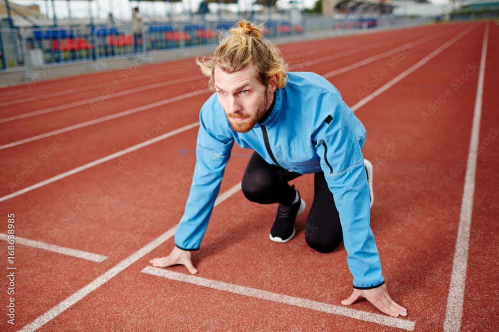 Ambitious athlete standing by starting line on stadium racetrack