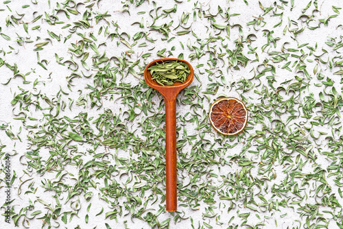 Wooden spoon and dry lemon slice on green tea leafs background.