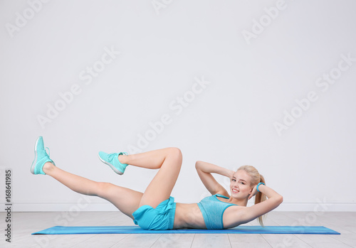 Sporty young woman training legs on mat in gym