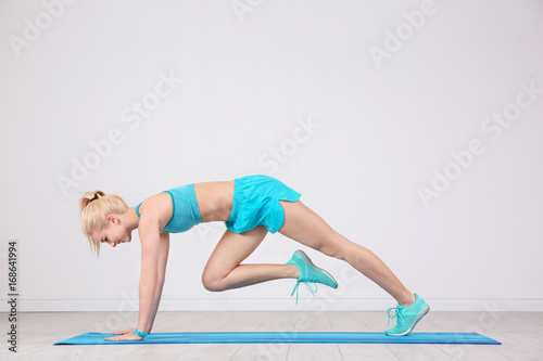 Sporty young woman training legs on mat in gym